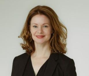 Dr Margaret Horton, a white woman with light brown highlighted hair wearing a black top and smiling directly into the camera